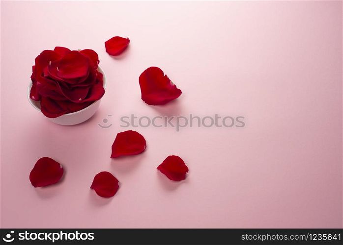 Beautiful red Rose petals in a white bowl and petals on the table on tender pink background. Rose petals used for perfumes, cosmetics and baths. Top view, copy space. Beautiful red Rose petals in a white bowl and petals on the table on tender pink background.