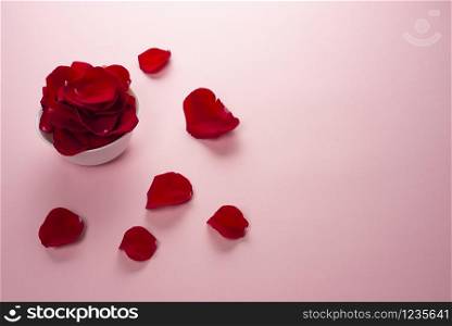 Beautiful red Rose petals in a white bowl and petals on the table on tender pink background. Rose petals used for perfumes, cosmetics and baths. Top view, copy space. Beautiful red Rose petals in a white bowl and petals on the table on tender pink background.