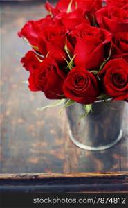 Beautiful red roses in a vase on wooden background