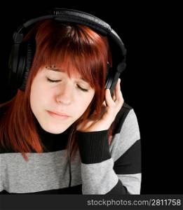 Beautiful redhead girl listening to music on headphones. Studio shot.