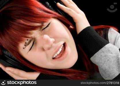Beautiful redhead girl singing while listening to her favorite music. Studio shot.