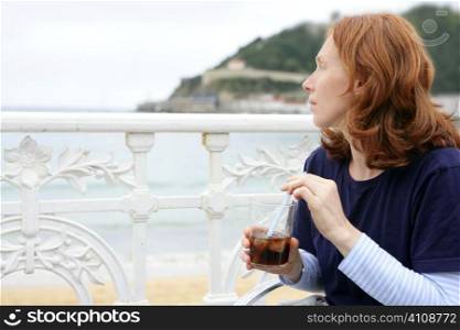 Beautiful redhead woman drinking beverage in La Concha beach San Sebastian