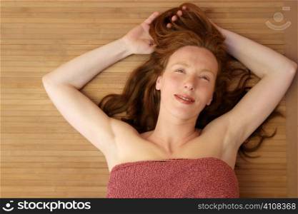 Beautiful redhead woman liying on bamboo in a golden spa center