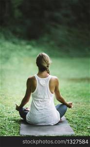 Beautiful relaxed young woman doing Yoga, sitting in half lotus position