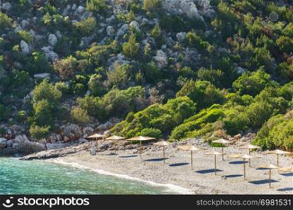 Beautiful rocky beach for tourists near cliff and sea water full of sun protecting umbrellas parasols.. Greek rocky beach with parasols