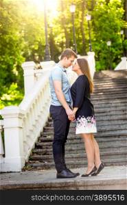 Beautiful romantic couple in love posing on stairs at park at sunny day