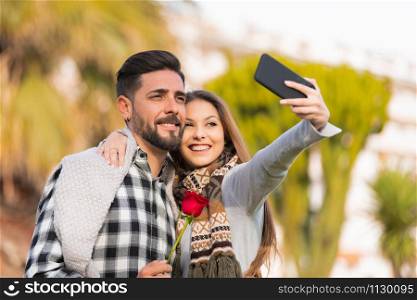 Beautiful romantic couple smiling while making selfie on a smart phone. Saint valentine&rsquo;s day concept.. Romantic couple smiling while making selfie