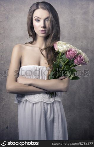 Beautiful, romantic, natural, young girl with curly, messy hair and white long dress holding a bouquet of roses.