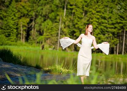 Beautiful romantic woman in summer sunny nature wearing white dress by lake