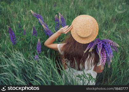 Beautiful romantic woman with bouquet of lupines joyfully in white dress and hat sits in field of purple lupine flowers. Soft selective focus.. Beautiful romantic woman with bouquet of lupines joyfully in white dress and hat sits in field of purple lupine flowers. Soft selective focus