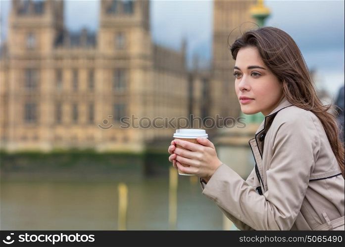 Beautiful sad, depressed or thoughtful young woman in London on Westminster Bridge over the River Thames drinking takeout coffee by Big Ben