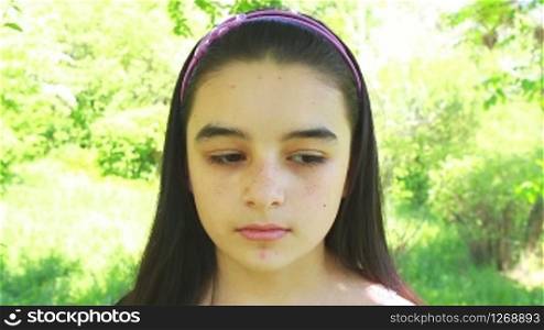 Beautiful sad teenage girl, against green of summer park.