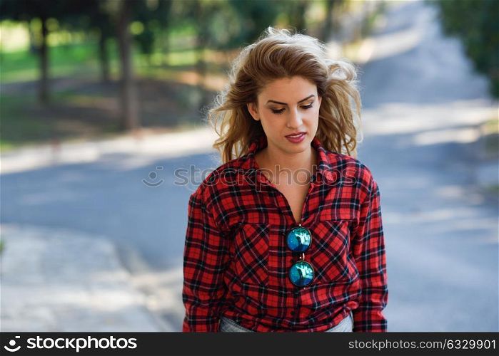 Beautiful sad young woman in the park. Girl with long blonde curly hair.