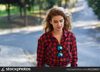 Beautiful sad young woman in the park. Girl with long blonde curly hair.