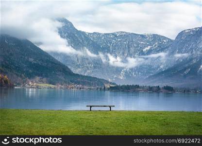 Beautiful scenery with the majestic Northern Limestone Alps, the Hallstatter lake and a wooden bench on its shore, in the famous Hallstatt town, in Austria.