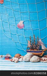 Beautiful sea composition with toy sailboat, seashell, glass bottle and fishing net on blue background. Sea interior decorations