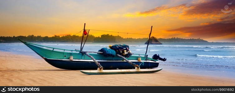 Beautiful seascape. Against the background of the sunset sky and the ocean, an old fishing boat. Sri Lanka. Wide photo.