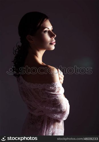 Beautiful seductive girl wearing sexy white lace night dress posing in the studio over dark background, stunning look, gentle sensual woman