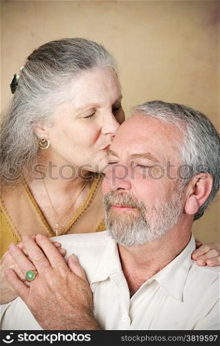 Beautiful senior woman gives her husband a loving kiss on the forehead. Vignette added for dramatic effect.