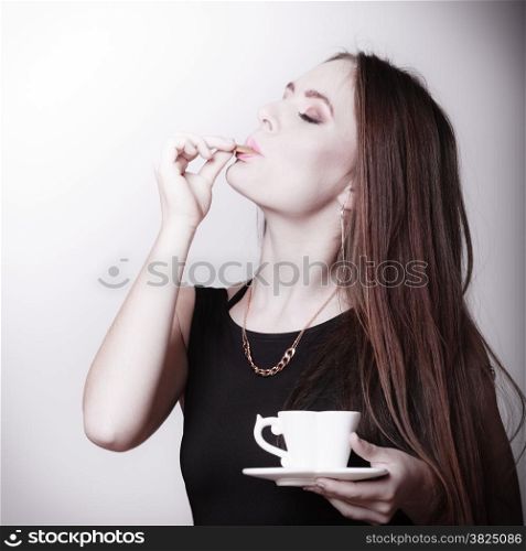 Beautiful sexy girl holding cup of coffee drinking eating cookie on gray