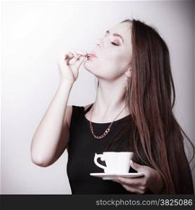 Beautiful sexy girl holding cup of coffee drinking eating cookie on gray