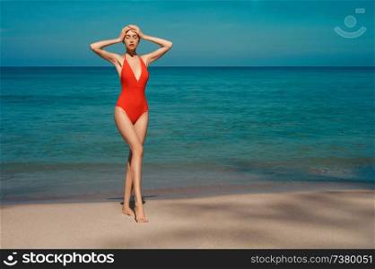 Beautiful sexy lady on tropical beach. Fashionable woman with slim perfect figure walking in front of blue sea. Model pose in red swimwear near the ocean. Relax portrait of young sunbathing beauty