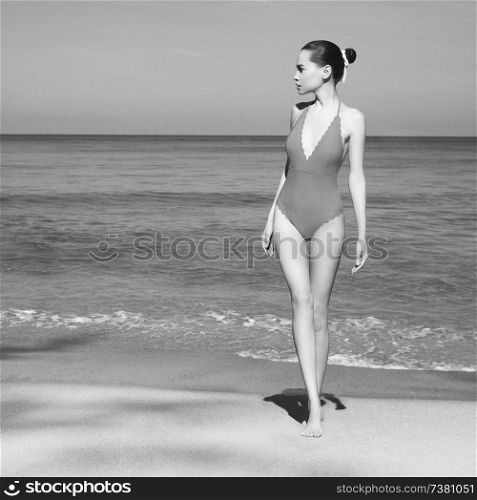 Beautiful sexy lady on tropical beach. Fashionable woman with slim perfect figure walking in front of sea. Model pose in retro swimwear near the ocean. Relax portrait of young sunbathing beauty