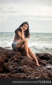 Beautiful sexy woman sitting on rock in the beach.