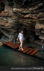 Beautiful sexy woman walking on wooden path at sea cave