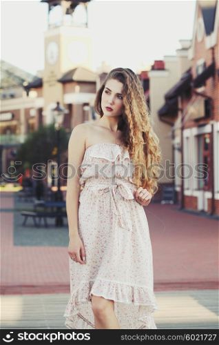 Beautiful sexy young blonde girl with long thick wavy hair thin slender figure perfect body and pretty face make-up wearing a light pink dress