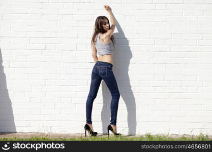 Beautiful sexy young brunette in blue jeans on white brick wall