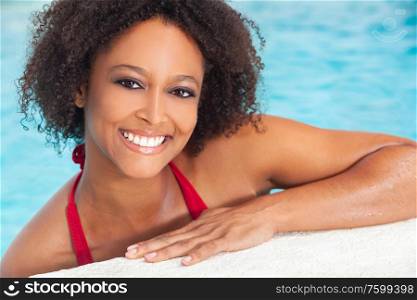 Beautiful sexy young mixed race African American girl or young woman with perfect teeth, wearing a red bikini and relaxing on the side of a swimming pool.