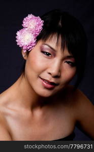Beautiful shaded face of an Asian-American woman with purple pink white flowers in her hair.
