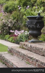 Beautiful shallow depth of field image of English country garden with urn style planter with flowers