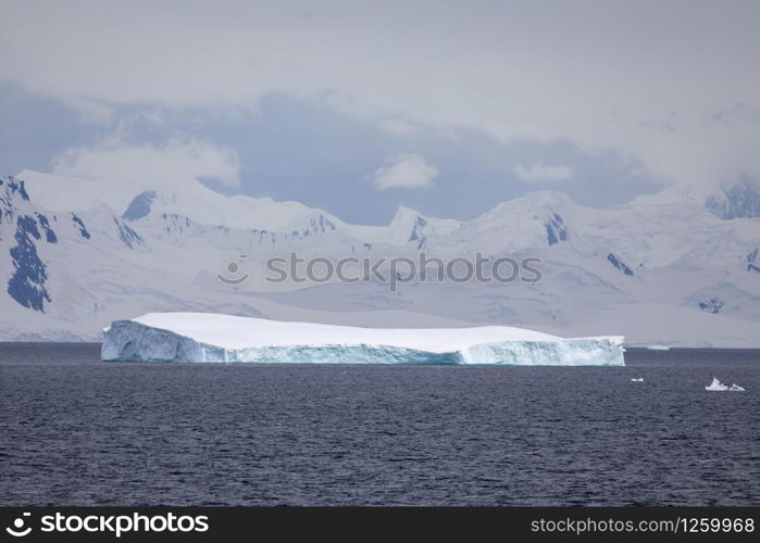 Beautiful shimmering blue iceberg swims in front of foggy mountains in the sea