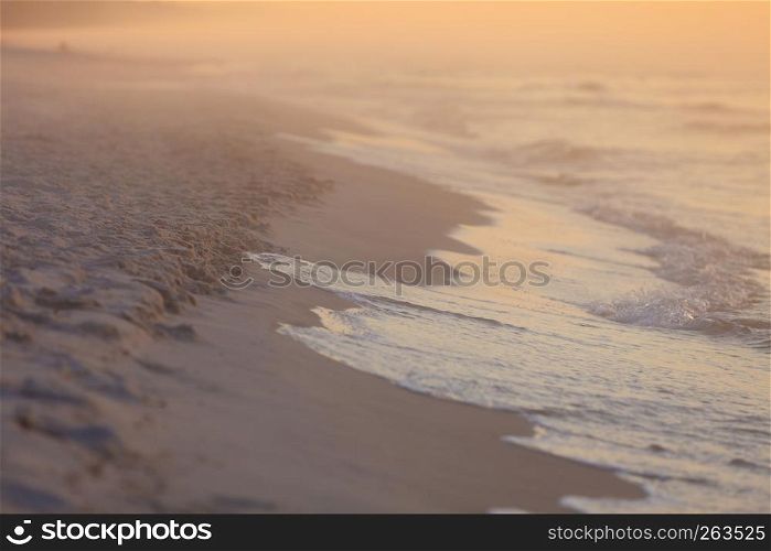 Beautiful shot of coastline landscape and man on a walk. Beach during morning foggy weather, milky orange colors.. Beach during sunrise fog