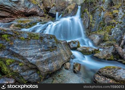 Beautiful shot of waterfall in Altai mountains in Siberia, Russia. Smooth, silky water. Long exposure. Rocks and logs in the foreground.. Beautiful shot of waterfall in Altai mountains in Siberia, Russia. Smooth, silky water. Long exposure. Rocks and logs in the foreground