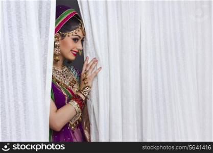Beautiful shy bride standing amidst curtains