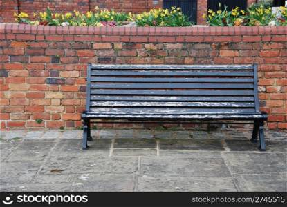 beautiful sidewalk scene with wooden bench, brick wall and flowers