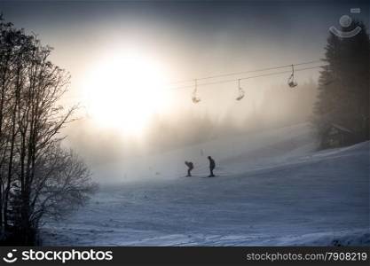 Beautiful silhouette photo of riding skiers and ski lift against bright winter sun