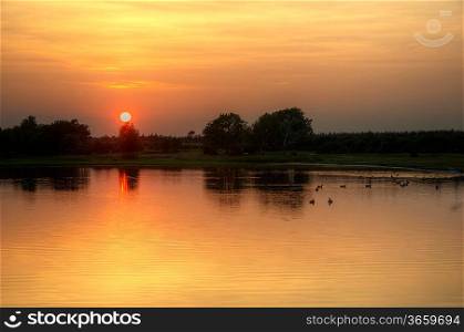 Beautiful simple image of sunset through tress reflected in lake in foreground