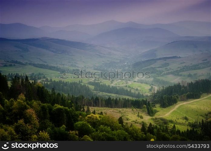 Beautiful sky and forest high up in Carpathian mountains. With view on village after rain with sunrays.