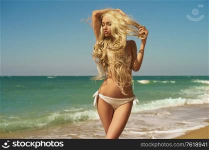 Beautiful slender blonde in white bikini. Summer travel photos of young sexy lady. Sunny day on the beach.