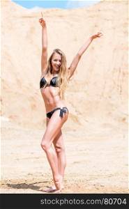 beautiful slender girl in a black bikini on the sand posing