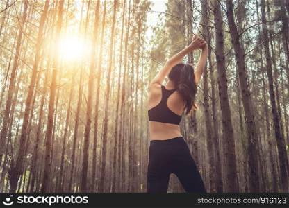 Beautiful slim female runner do stretching arms and warm up to running in peaceful forest in morning. Workout and exercise concept. Healthy in nature concept. Pine woods in autumn seasonal theme.