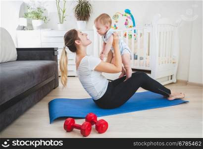 Beautiful slim mother playing with her baby on fitness mat at home