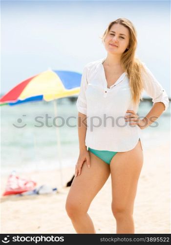 Beautiful slim woman in white shirt posing on beach against parasols