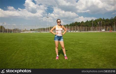 Beautiful slim woman standing on soccer field at sunny day
