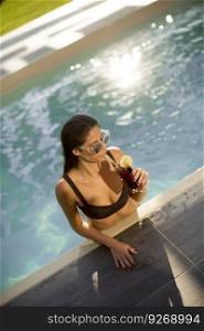 Beautiful slim young woman in bikini and sunglasses relaxing and drink cocktail on poolside of a swimming pool