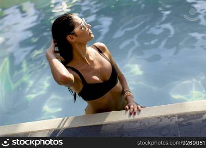 Beautiful slim young woman in bikini and sunglasses relaxing and sunbathing on poolside of a swimming pool